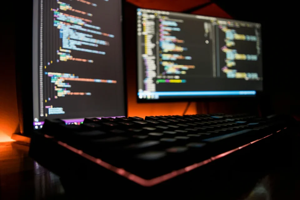 Two monitors displaying source code behind a keyboard.