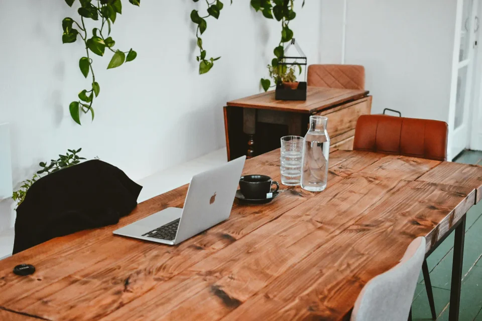 Laptop on a wooden table in a bright home workspace with plants.